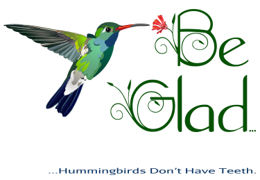 A stylized humming bird hovers near a flower in the stylized lettering of, “Be Glad…” Much smaller text below continues, “...Hummingbirds don’t have teeth.”